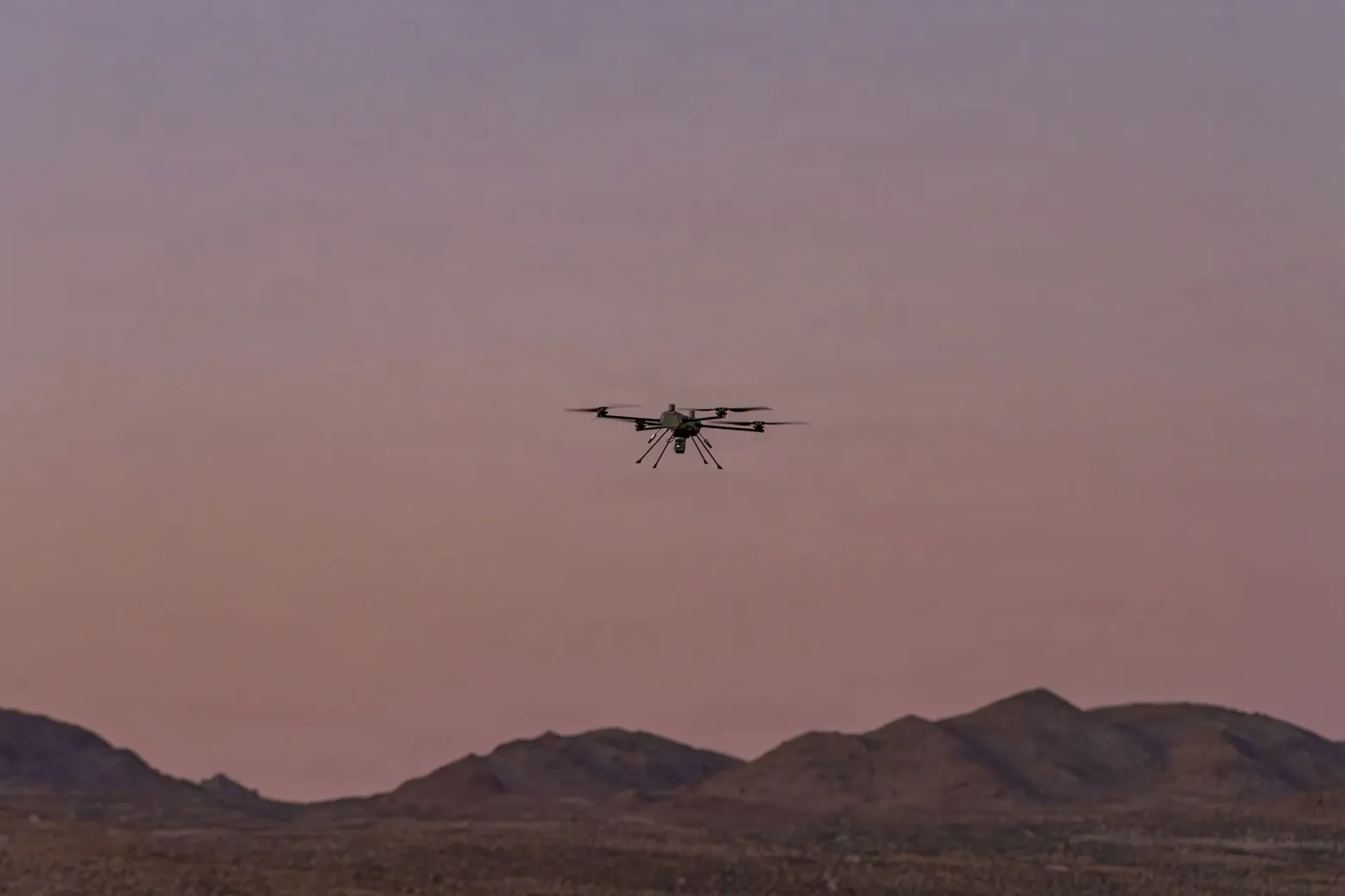 Фотография парящего в небе дрона на фоне горного хребта