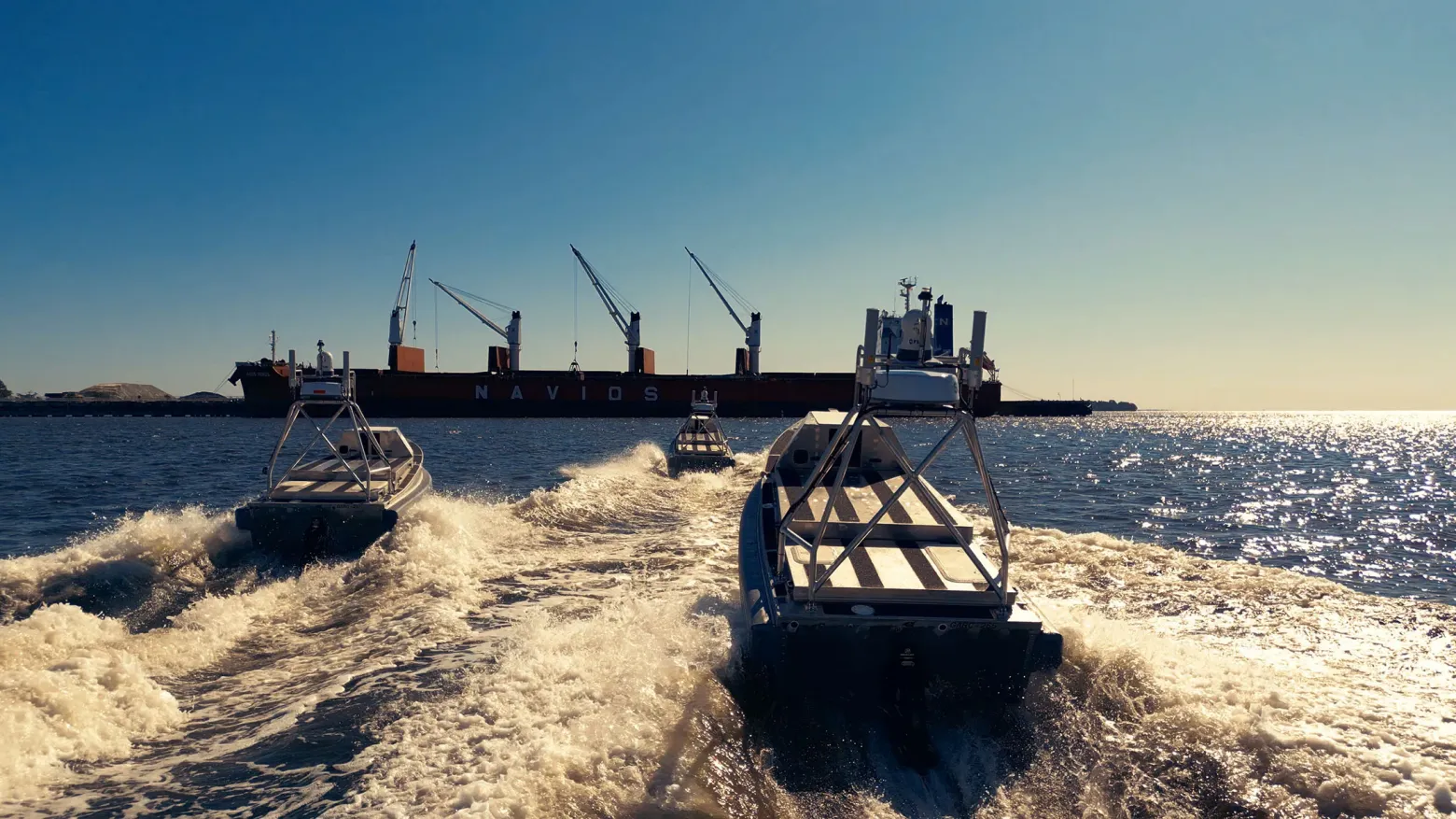 Три небольшие лодки в море приближаются к большому грузовому судну